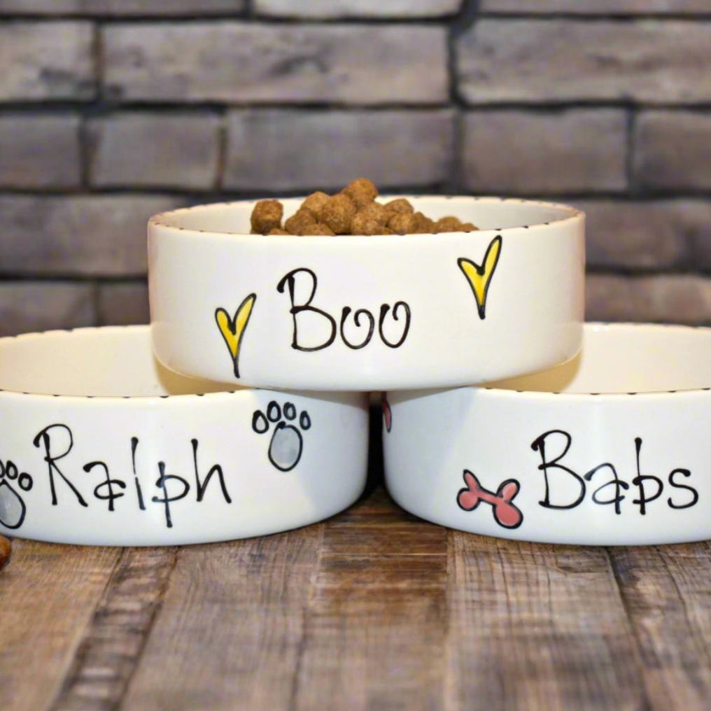 Three white pet bowls with names 'Boo', 'Ralph', and 'Babs' on a wooden surface.