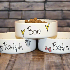 Three white pet bowls with names 'Boo', 'Ralph', and 'Babs' on a wooden surface.