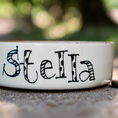 White ceramic bowl with 'Stella' written on it, placed outdoors.