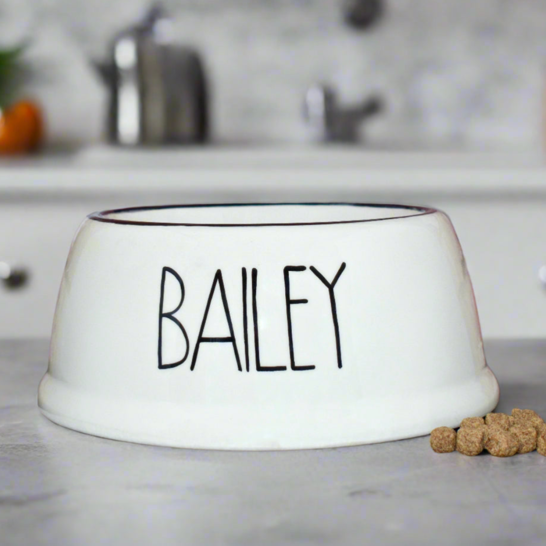 White pet bowl with 'BAILEY' printed on it, placed on a kitchen counter.