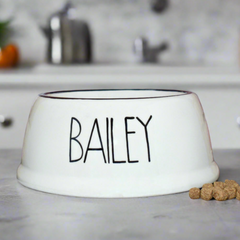 White pet bowl with 'BAILEY' printed on it, placed on a kitchen counter.